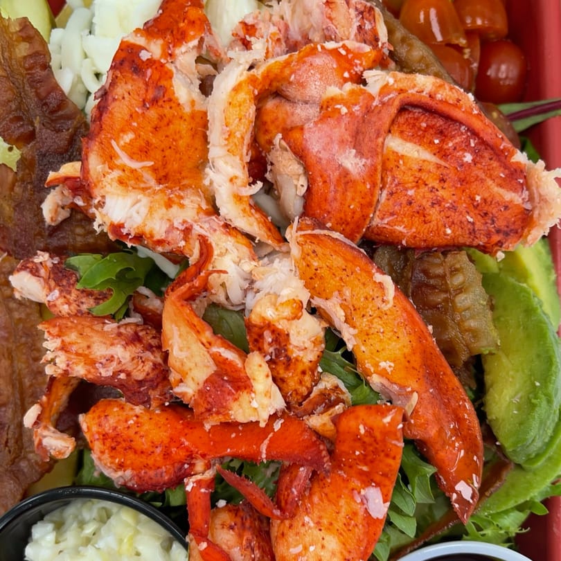 Close-up of a Mystic Lobster Roll Co. lobster salad with avocado, bacon, and cherry tomatoes.