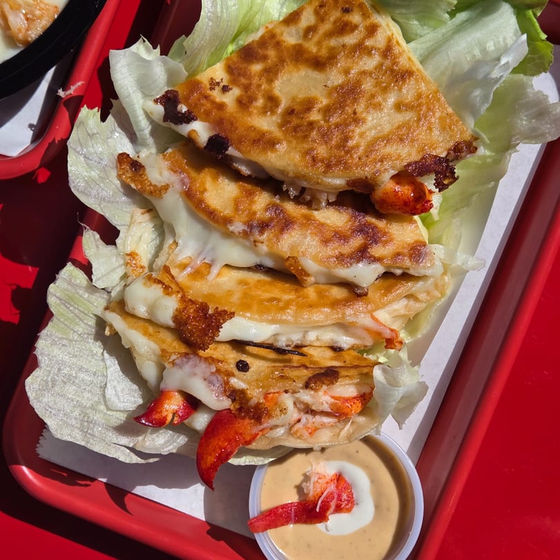 Mystic Lobster Roll Co.'s lobster quesadillas with melted cheese, lettuce, and dipping sauce on a red tray.