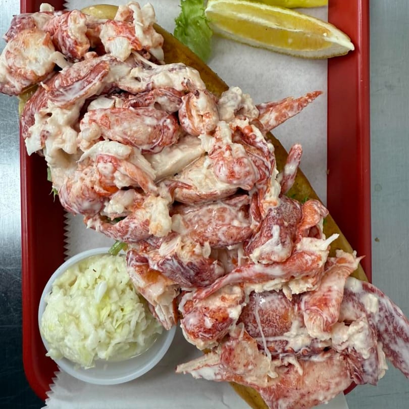 A Mystic Lobster Roll Co. lobster roll overflowing with meat, served with coleslaw and lemon.