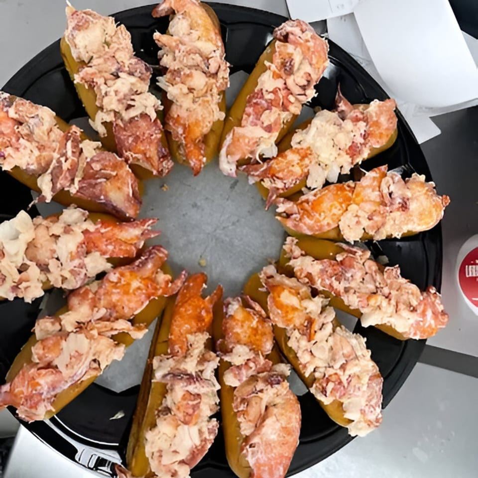 A black platter holds a dozen lobster rolls arranged in a circle, filled with fresh lobster meat.