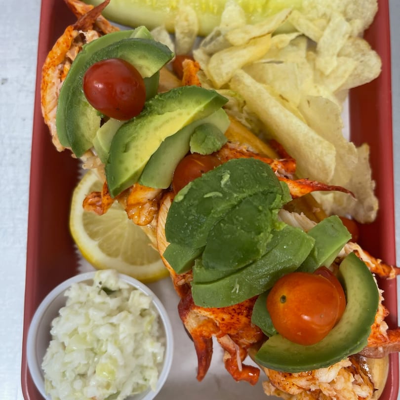 Mystic Lobster Roll Co's lobster roll with avocado, cherry tomatoes, lemon, coleslaw, and chips.